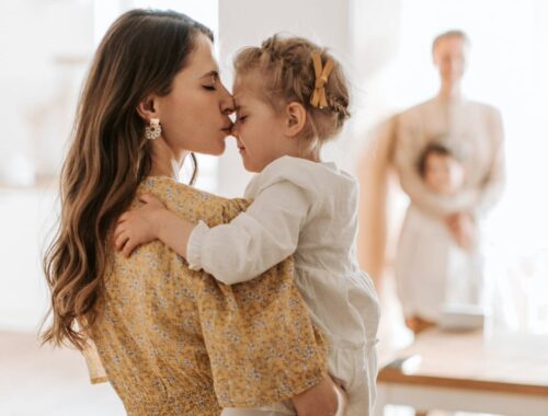 Kobieta całuje swoją córkę w czoło trzymając ją na rękach