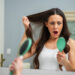 Kobieta z wypadającymi włosami stoi w łazience przed lustrem